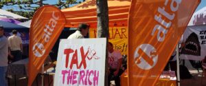 Infostand von Attac Düsseldorf mit Beachflages mit der Aufschrift "attac" und einem Plakat mit der Aufschrift "Tax the Rich".