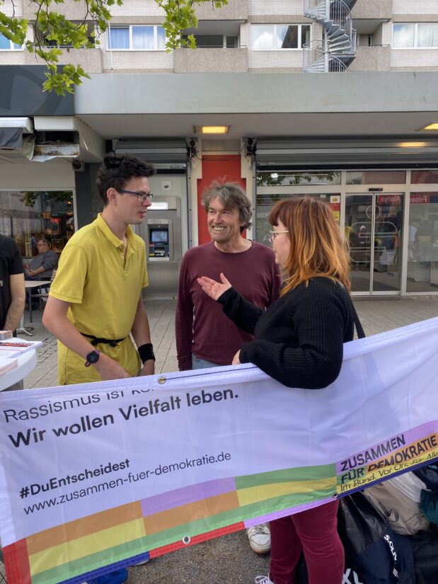 Banner "Wir wollen Vielfalt leben" und Aktive von teilnehmenden Initiativen im Gespräch